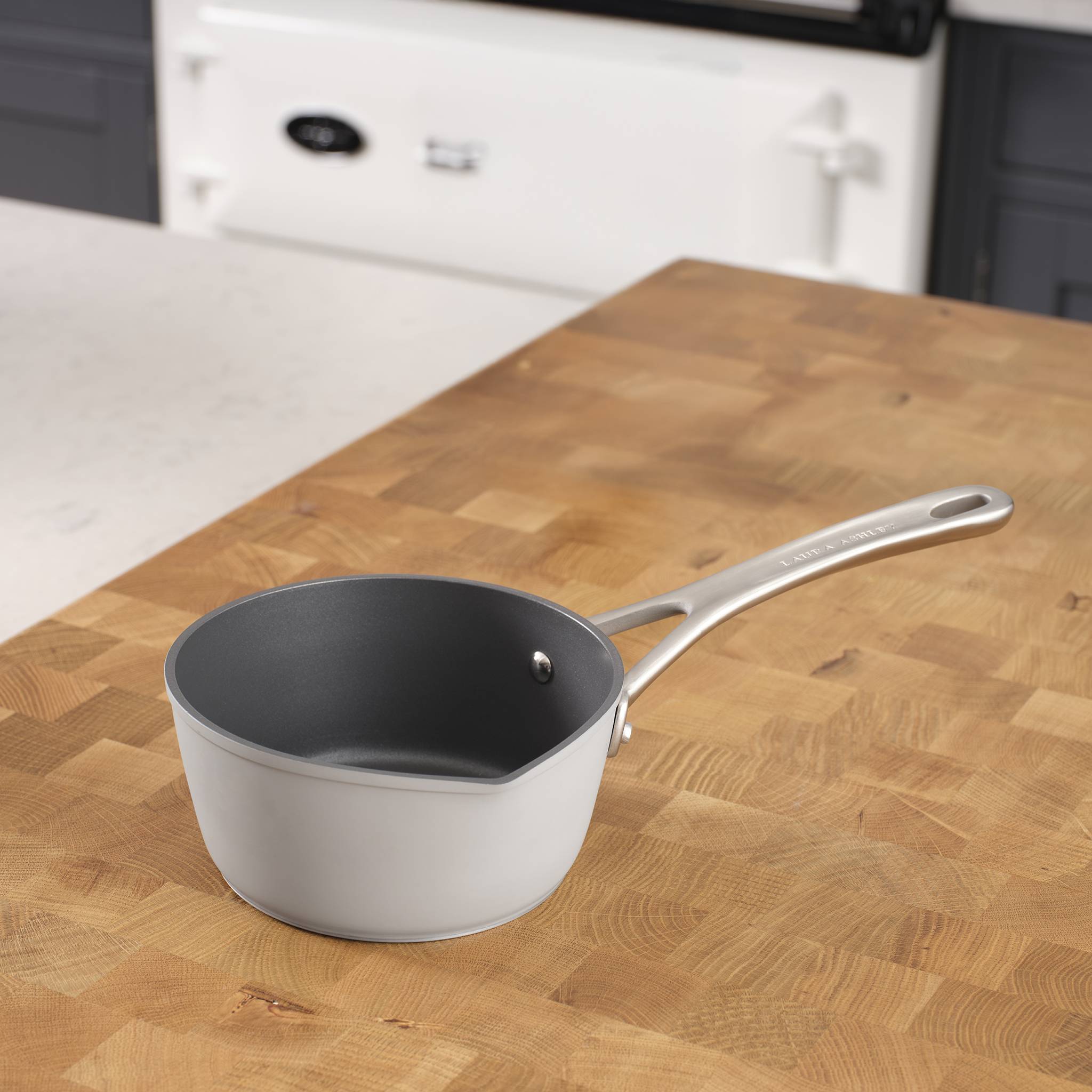 Eine graue Pfanne mit Griff ruht auf einer hölzernen Küchenarbeitsplatte, mit einem weißen Herd im Hintergrund.