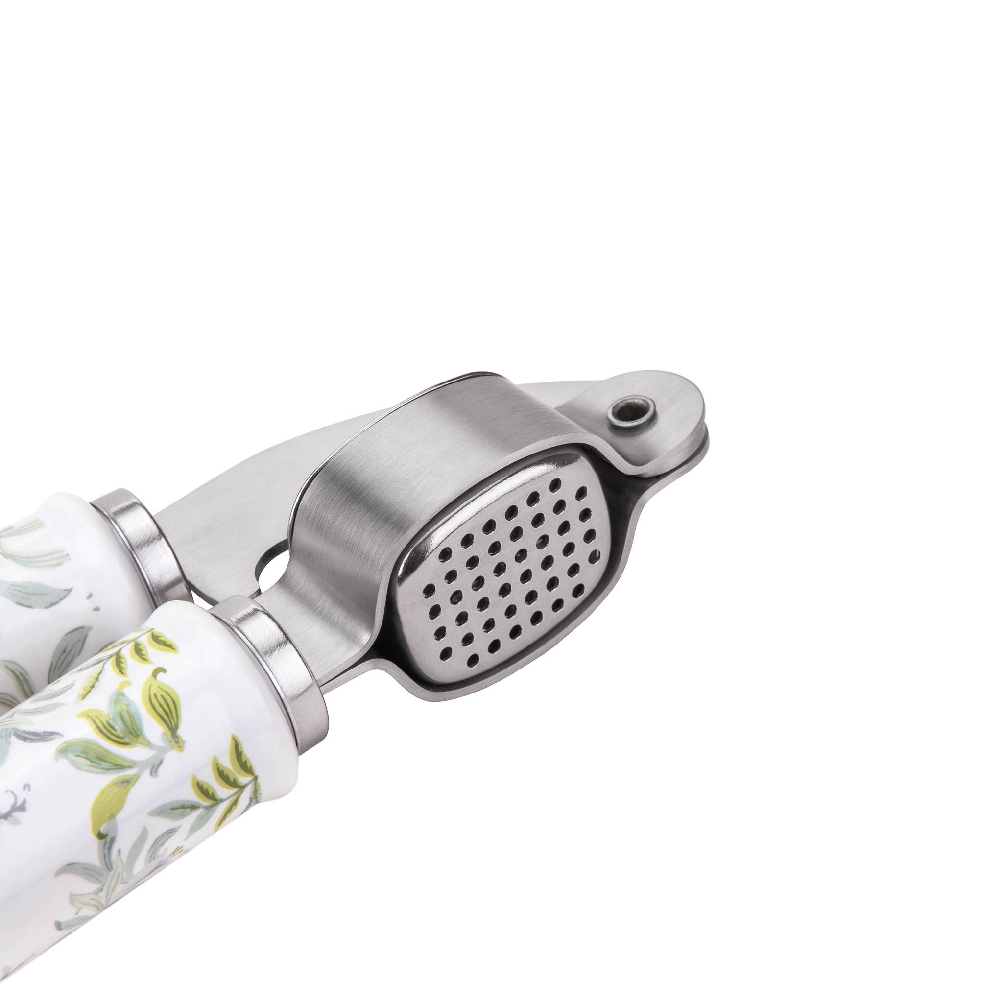 Eine Knoblauchpresse aus Metall mit weißen Griffen, die ein grünes und gelbes Blatmuster zeigen, zum Zerdrücken von Knoblauchzehen entworfen.