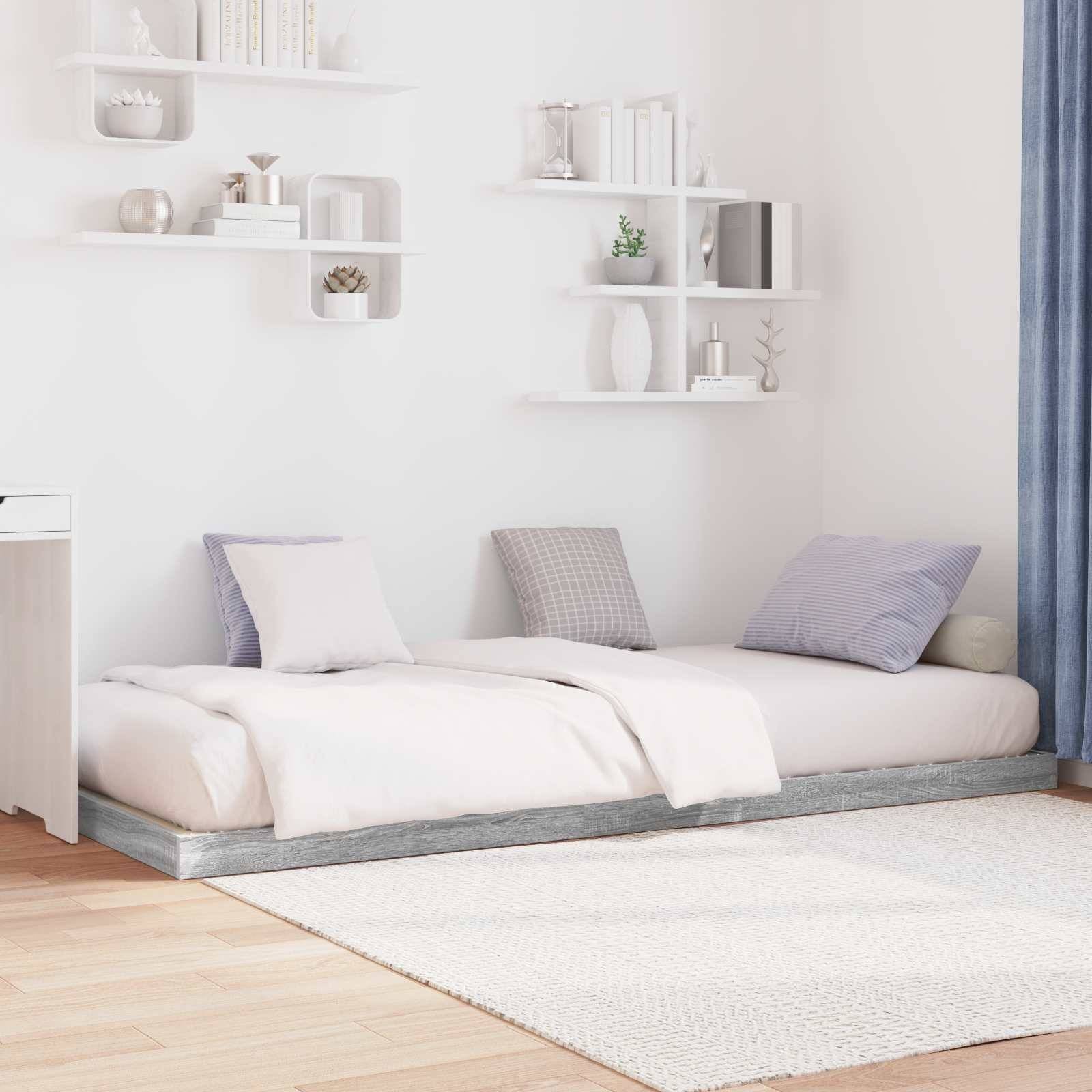Minimalistisches Schlafzimmer mit einem niedrigen Bett, weißer Bettwäsche, grauen und blauen Kissen. Weiße Regale an der Wand über dem Bett zeigen Dekoration.