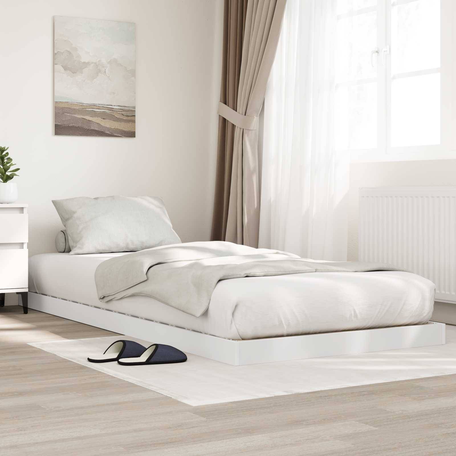 Ein minimalistisches Schlafzimmer mit einem flachen Plattformbett, neutraler Bettwäsche, Nachttisch, Lampe, gerahmetem Kunstwerk und lichtdurchlässigen Vorhängen.