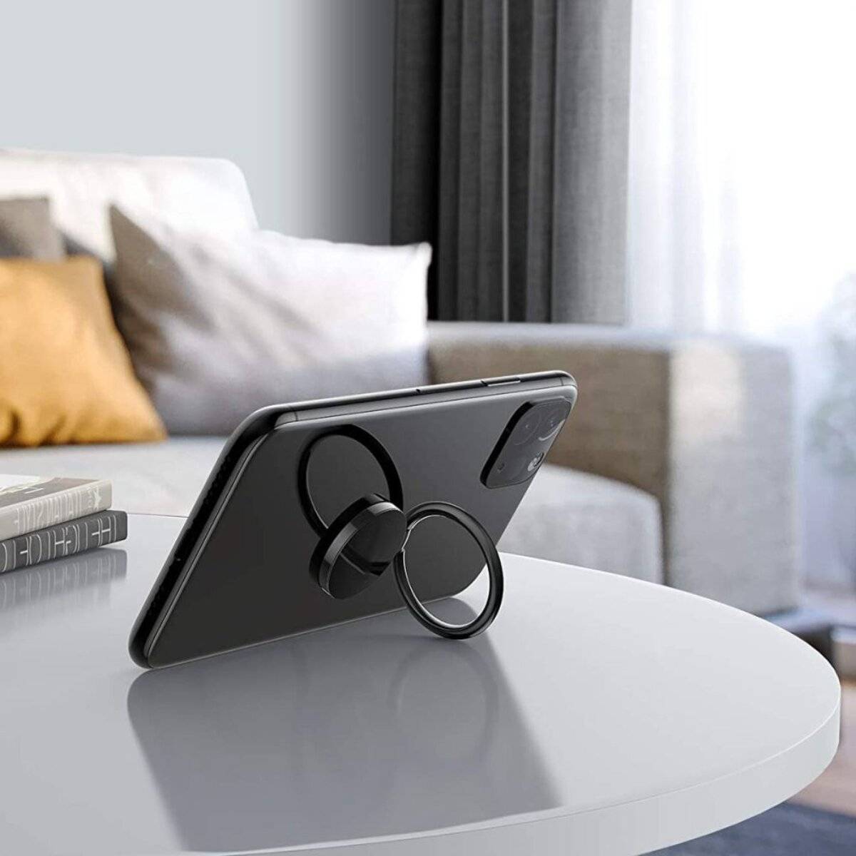 Ein Smartphone mit einem Ringständer wird aufrecht geneigt auf einem weißen runden Tisch platziert. Ein beigefarbenes Sofa und Kissen sind im Hintergrund.