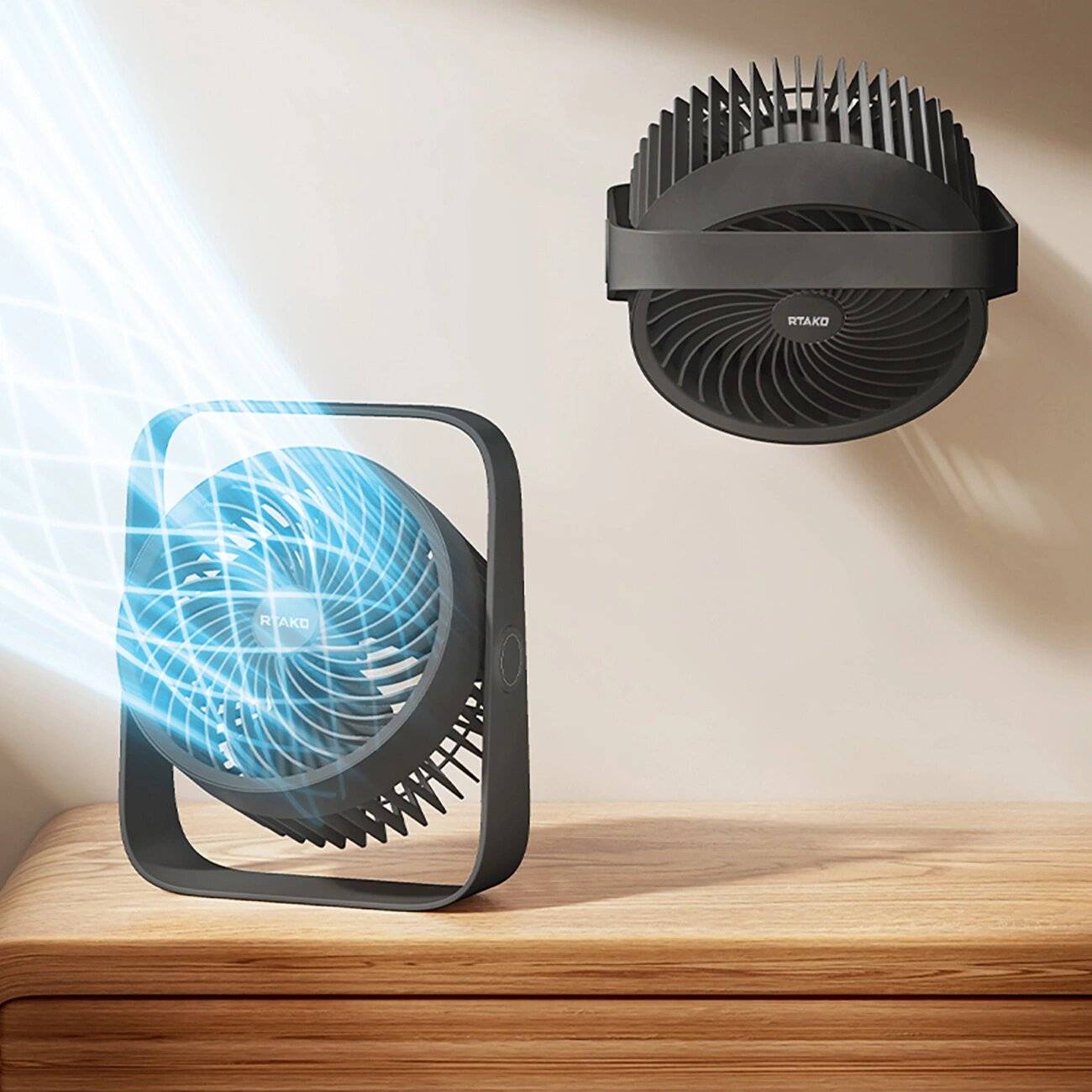 Ein wandmontierter Ventilator und ein Tischventilator stehen auf einem Holztisch. Beide Ventilatoren haben schwarze Rahmen und geben einen sichtbaren Luftstrom ab.