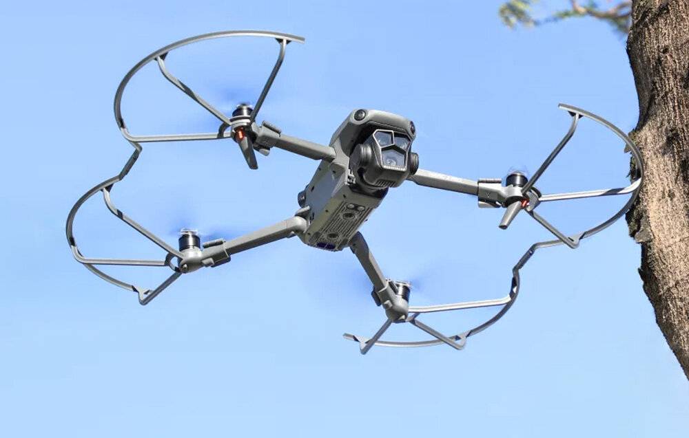 Eine Quadcopter-Drohne mit Kamera schwebt in der Luft gegen einen klaren blauen Himmel und betont ihr technisches Design und ihre Luftfahrtfähigkeit.