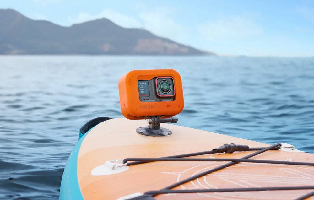 Kamera, die auf einem orangefarbenen Schwimmer oben auf einem Paddleboard montiert ist, mit einer malerischen Aussicht auf Wasser und Berge im Hintergrund.