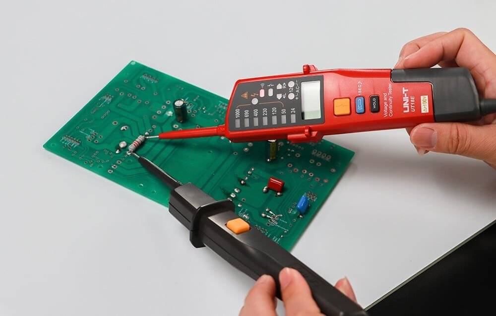 Eine Person verwendet ein digitales Multimeter, um eine elektronische Schaltung auf einer Leiterplatte zu testen und misst die Spannung über Widerstände auf einer grünen Leiterplatte.