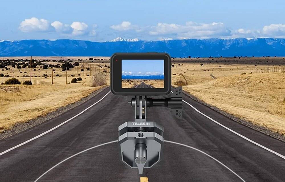 Eine auf einer Halterung montierte Kamera fokussiert auf eine gerade, leere Straße, die in Richtung entfernter Berge unter einem blauen Himmel führt.