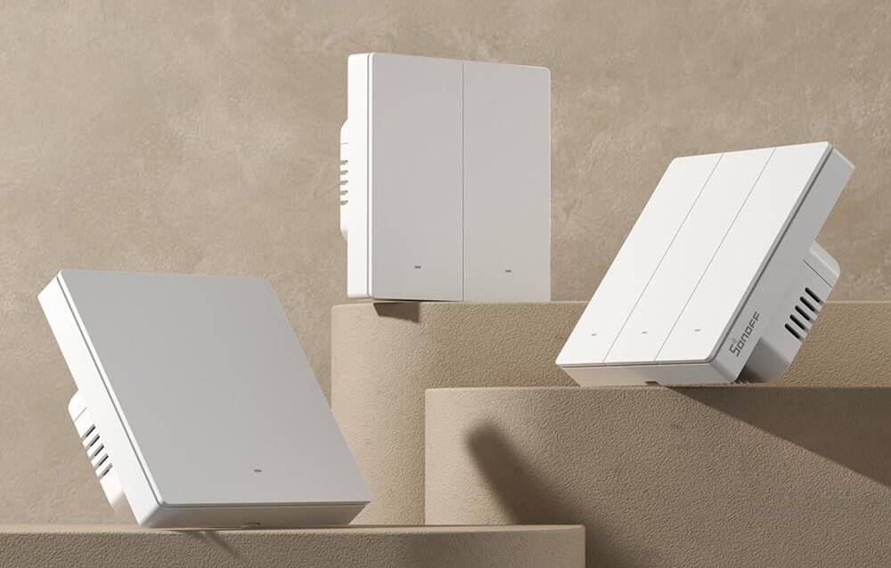 Drei weiße, minimalistische Lautsprecher in verschiedenen Größen sind auf gestuften beigen Plattformen ausgestellt und werfen Schatten auf den neutralen Hintergrund.