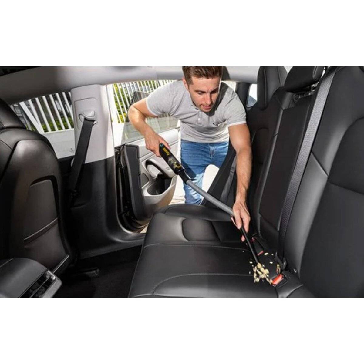 Eine Person, die mit einem tragbaren Staubsauger den Rücksitz eines Autos absaugt und sich auf die Reinigung der schwarzen Lederpolsterung konzentriert.