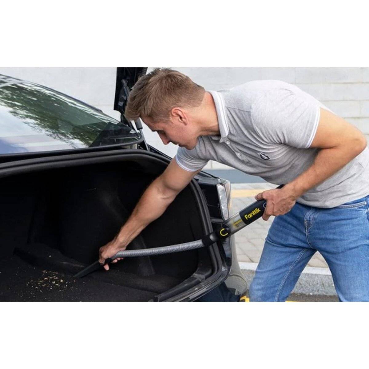 Eine Person benutzt einen tragbaren Handstaubsauger, um den Kofferraum eines Autos zu reinigen, wobei sie sich auf die Entfernung von Verschmutzungen und Schmutz von der Innenfläche konzentriert.