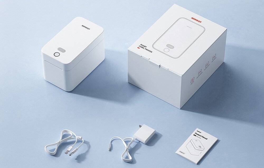 Kompakter weißer Thermodrucker mit Karton, USB-Kabel und Anleitung auf hellblauer Oberfläche.