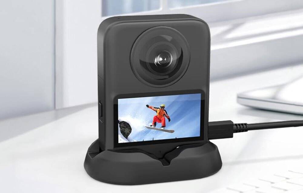 Eine Kamera auf einer Ladestation mit einem Bildschirm, der einen Snowboarder mid-Jump gegen eine verschneite Bergkulisse zeigt.