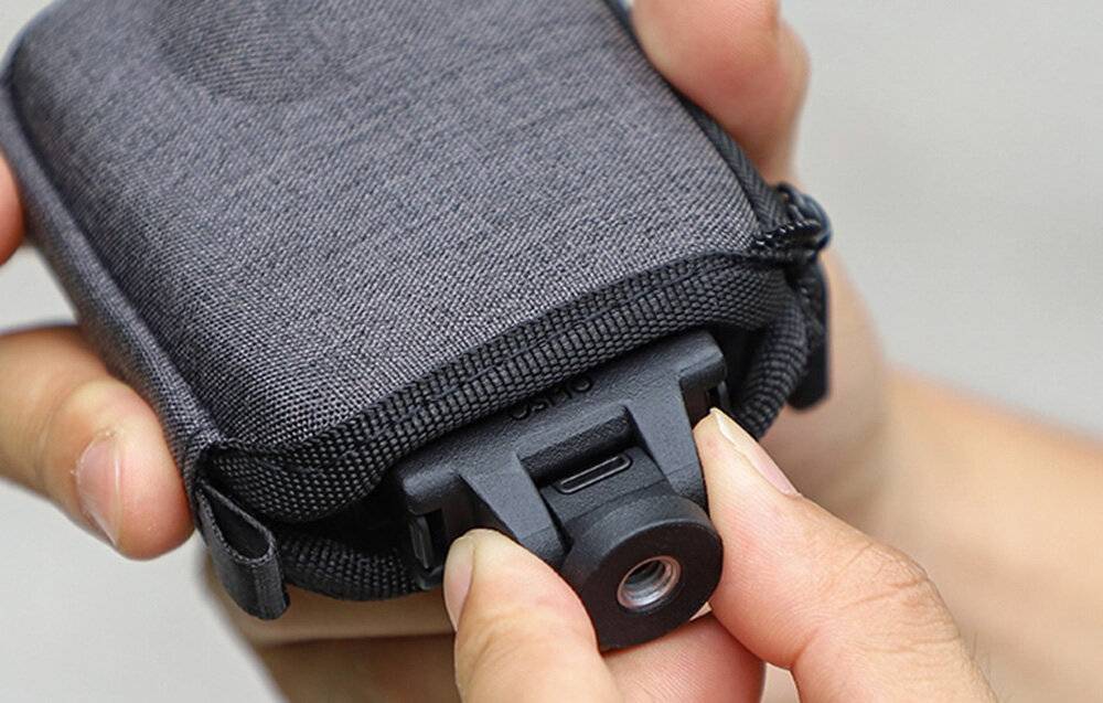 Eine Nahaufnahme einer Hand einer Person, die einen Knopf auf einem kleinen, grauen Mesh-Beutel mit Gürtelclip drückt.