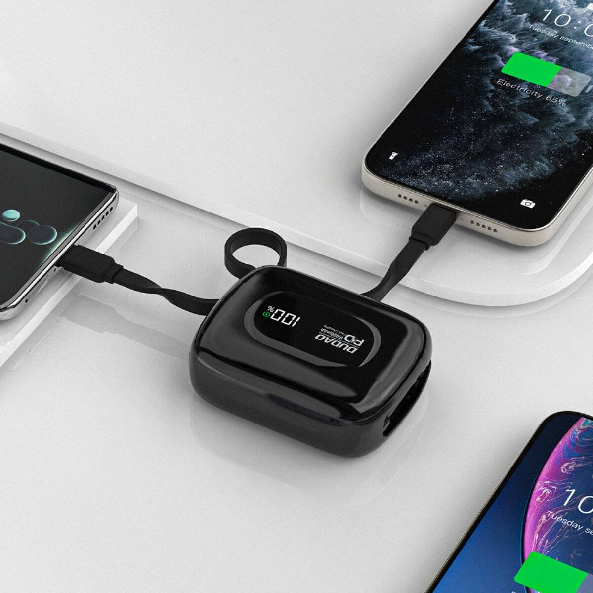 Ein schwarzes Powerbank mit LED-Display, das den verbleibenden Batteriestand in Prozent anzeigt, lädt zwei Smartphones auf einer weißen Oberfläche auf.