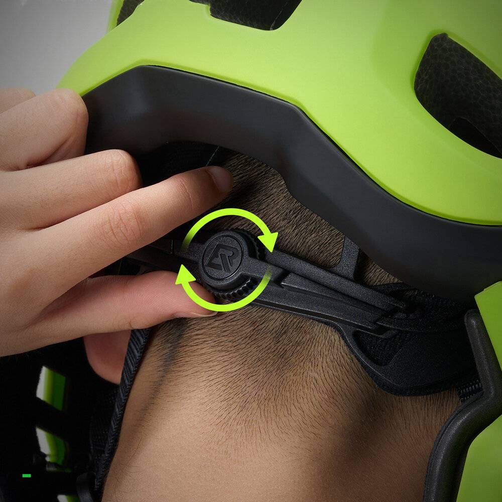 Eine Nahaufnahme einer Person, die die Passform eines grünen Fahrradhelms anpasst, wobei eine Hand das Einstellrad auf der Rückseite dreht.