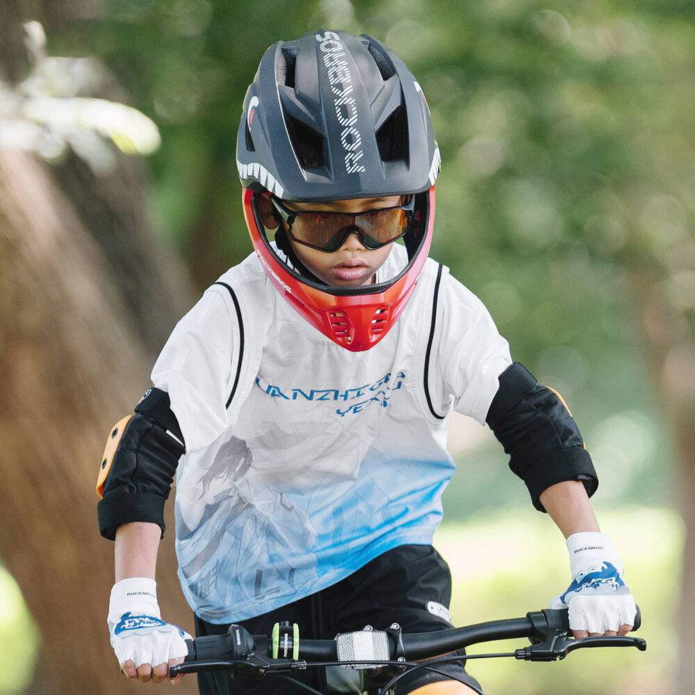 Ein Kind mit Helm, Sonnenbrille und Fahrradkleidung fährt konzentriert auf einem Fahrrad. Bäume bilden einen unscharfen grünen Hintergrund.