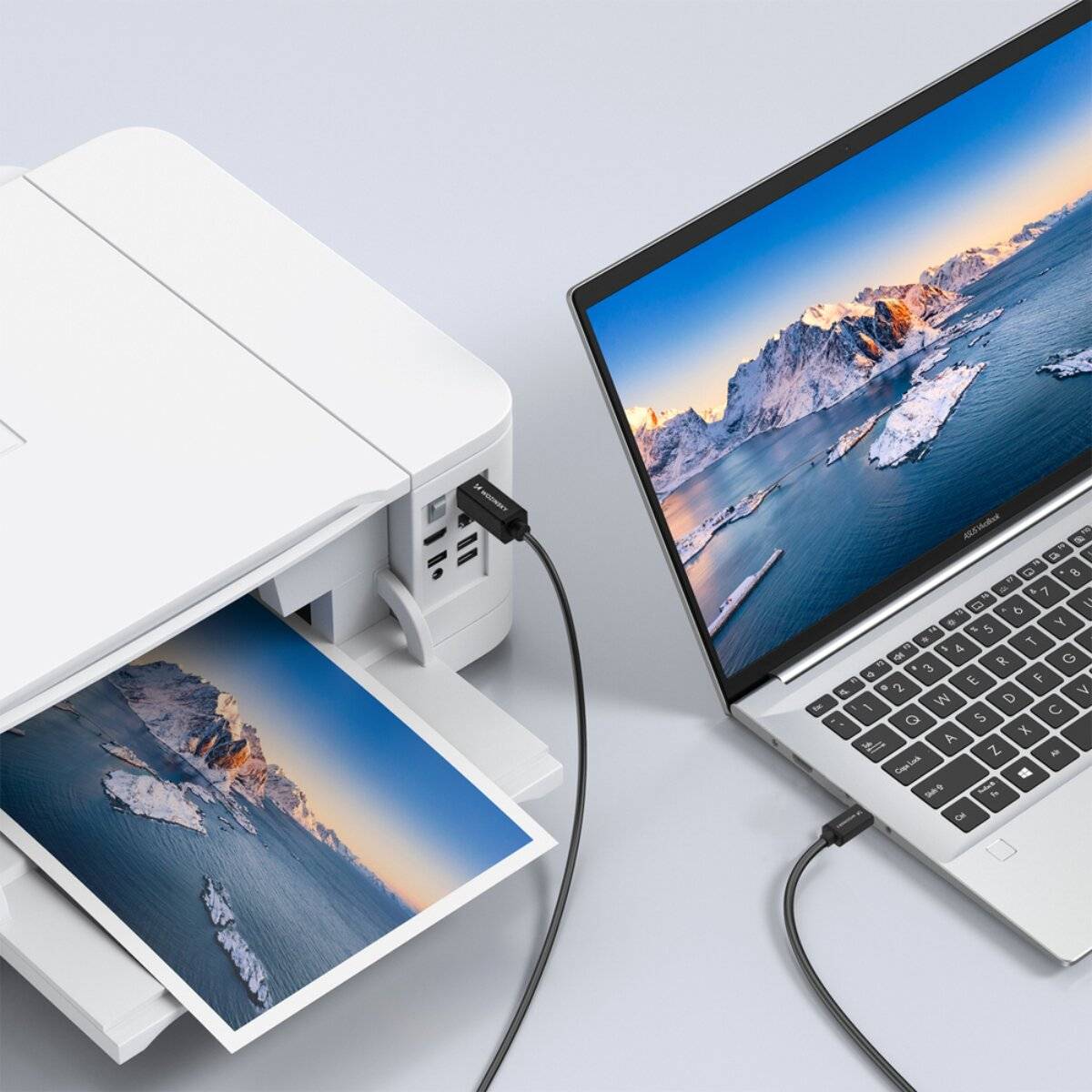 Ein Laptop, auf dem eine Berglandschaft angezeigt wird, ist mit einem Drucker verbunden, der dasselbe Bild druckt und veranschaulicht so eine nahtlose Geräteintegration.