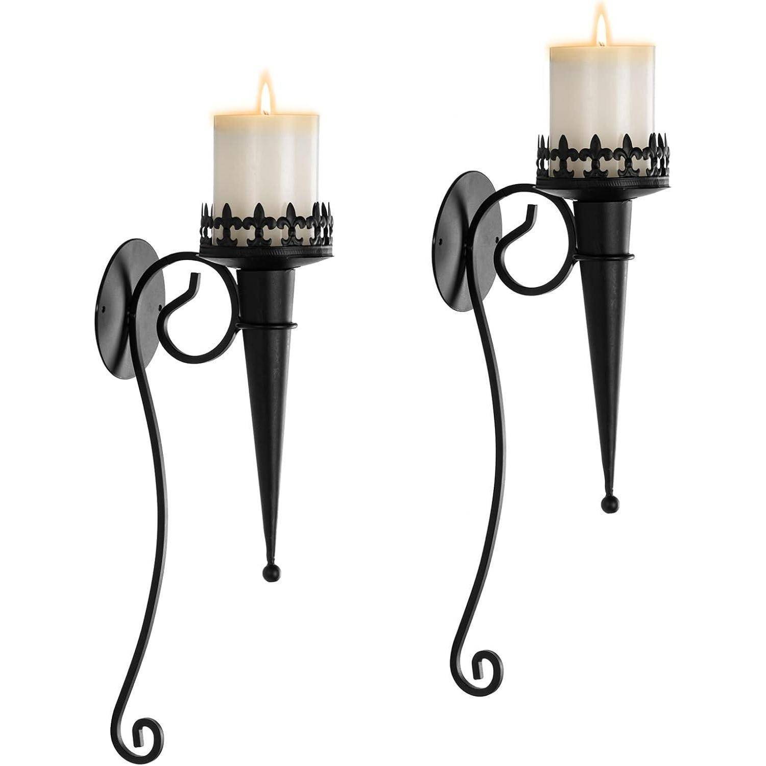 Zwei verzierte schwarze Metallwandleuchter, jeweils mit einer brennenden weißen Kerze. Das Design umfasst aufwendige kronenähnliche Details um die Kerzenbasis.