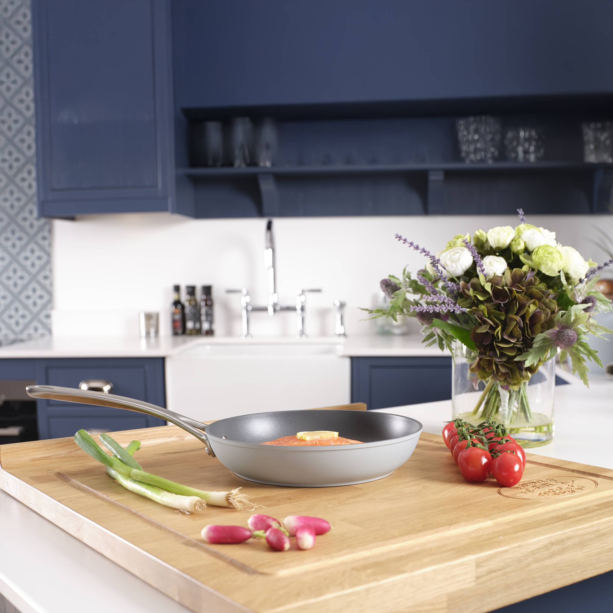 Eine moderne Küche mit blauen Schränken; eine Pfanne mit Gemüse auf einer Holzarbeitsplatte neben einem Blumenstrauß in der Nähe des Spülbeckens.