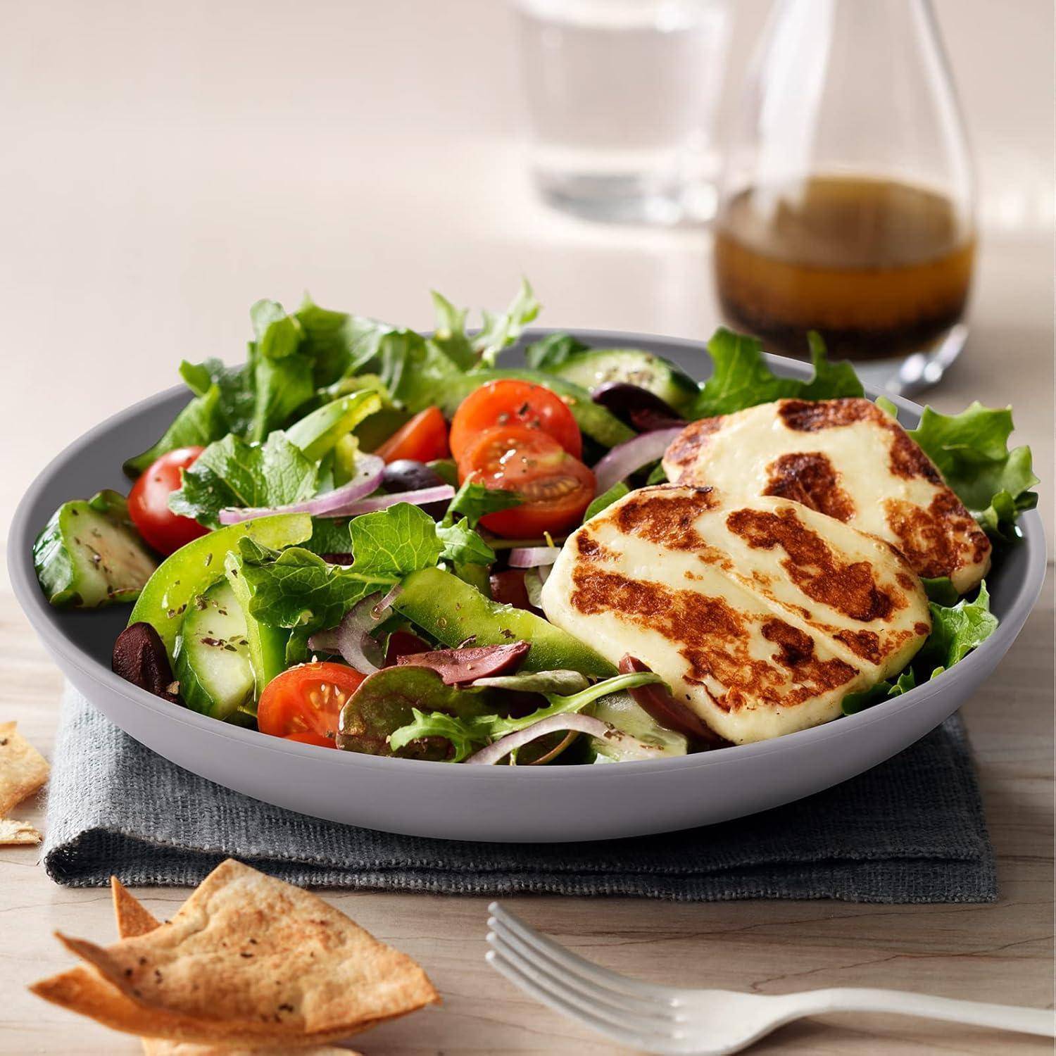 Ein frischer Salat mit Kirschtomaten, Gurke, roten Zwiebeln, gemischten Blattsalaten, Oliven und gegrilltem Halloumi, serviert mit Pitabrot.