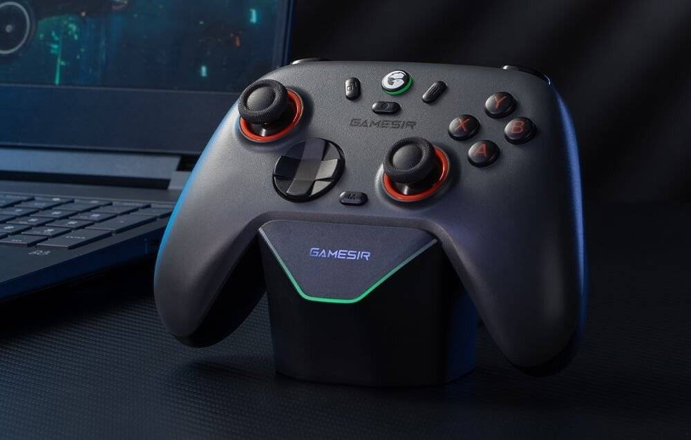 Ein schwarzer Gaming-Controller mit roten Akzenten von GameSir ruht auf einer Ladestation und ist neben einem teilweise sichtbaren Laptop platziert.