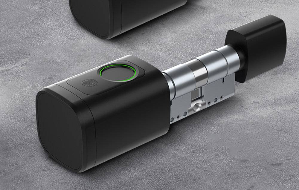 Ein intelligentes Schloss mit zylindrischem Design, das einen leuchtenden grünen Ring um seinen Fingerabdruckscanner aufweist, liegt auf einer grauen Oberfläche.