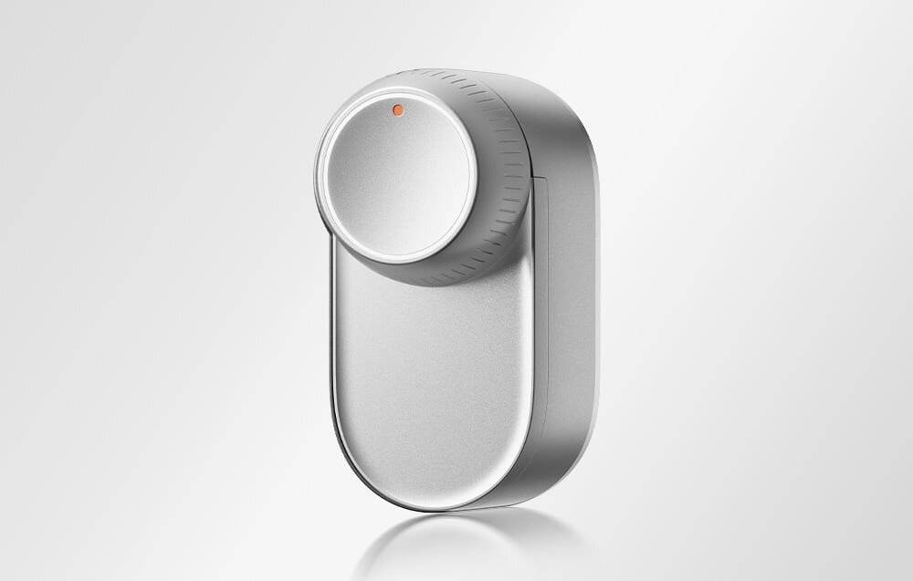 Ein schlankes, silbernes Smart-Lock mit einer kreisförmigen Bedienungswählscheibe und einer kleinen roten Anzeigelampe auf grauem Hintergrund.