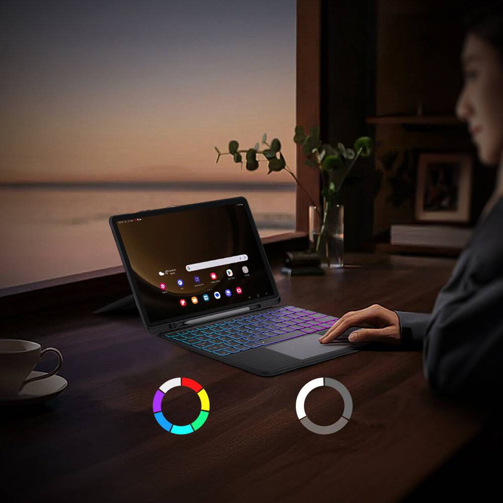 Eine Person nutzt einen Laptop mit bunten Tastaturbeleuchtungen auf einem Holzschreibtisch neben einem großen Fenster bei Sonnenuntergang, mit einer Tasse neben sich.