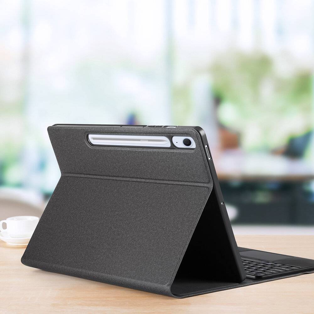 Ein schwarzes Tablet-Etui mit Ständerfunktion stützt ein Tablet auf einem Schreibtisch auf, mit einem unscharfen Hintergrund einer Büro- oder Haushaltsumgebung.