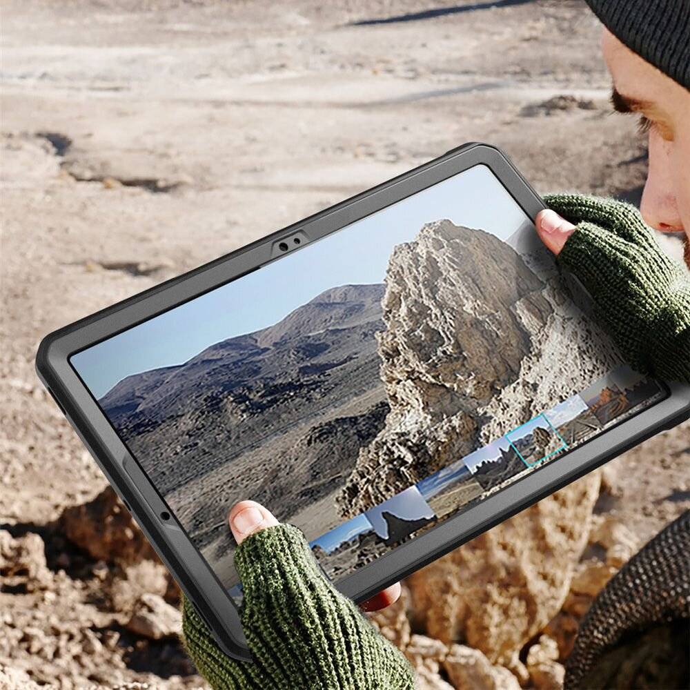 Eine Person mit Handschuhen hält ein Tablet, das eine große Felsformation in einer Wüstenlandschaft anzeigt, die die Szene im Hintergrund widerspiegelt.