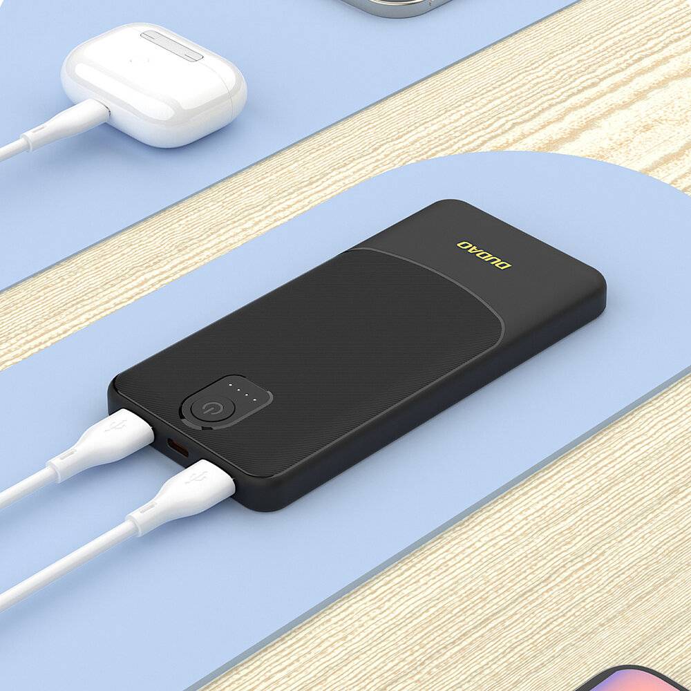 Ein schwarzes tragbares Powerbank mit zwei angeschlossenen Ladekabeln, auf einer hellblauen Oberfläche platziert, neben einem Paar kabellosen Kopfhörern.