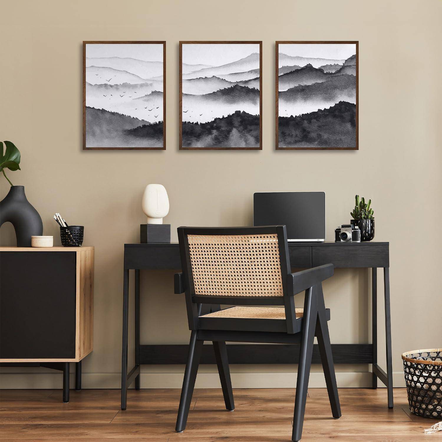Ein Homeoffice mit einem Holzschreibtisch und Stuhl. Ein Laptop, eine Lampe und eine kleine Pflanze stehen auf dem Schreibtisch. Drei gerahmte Berglandschaftsbilder hängen an der Wand.