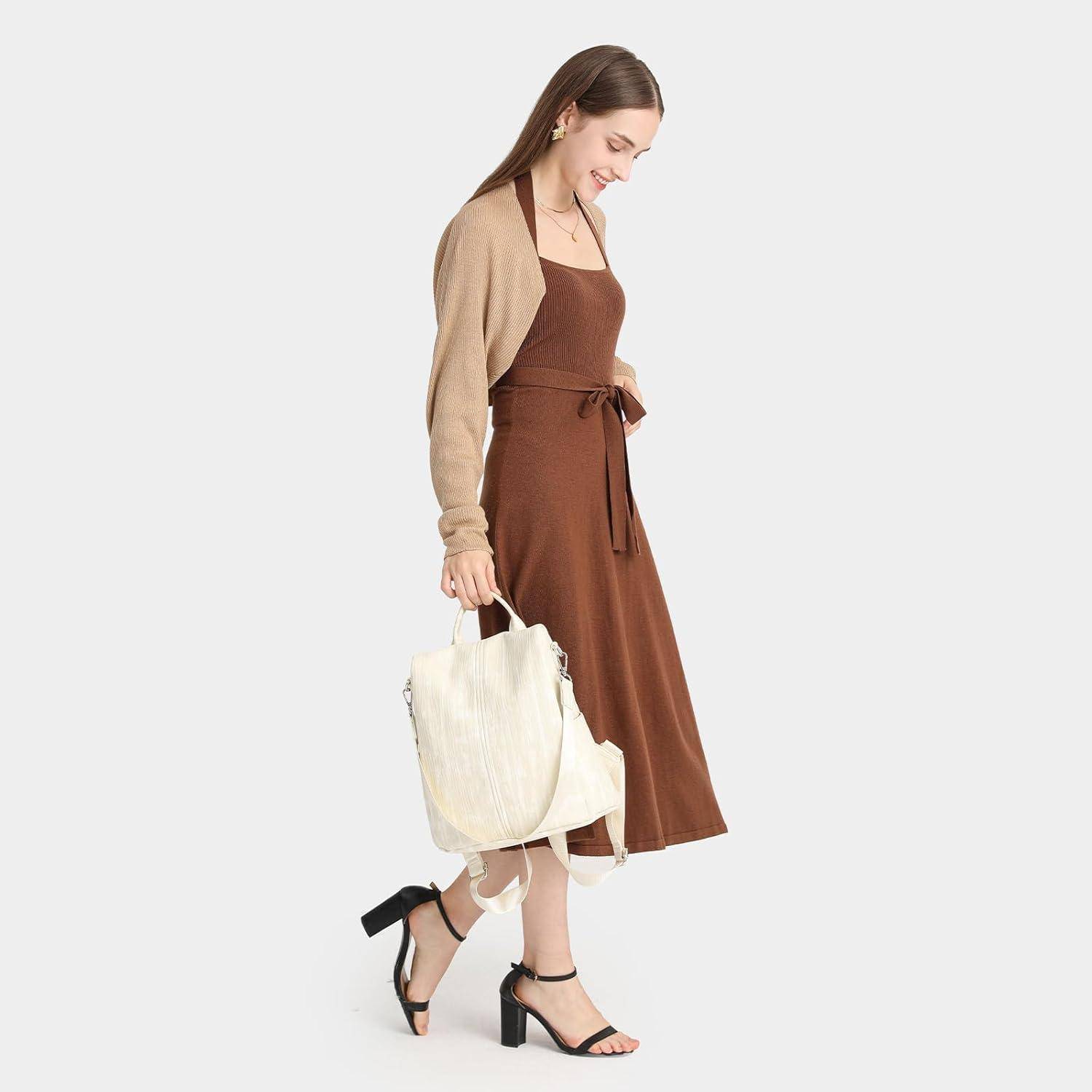 Eine Frau in einem braunen Kleid und einer beigen Strickjacke trägt eine große weiße Tragetasche und geht mit großem Schritt gegen einen einfachen Hintergrund.