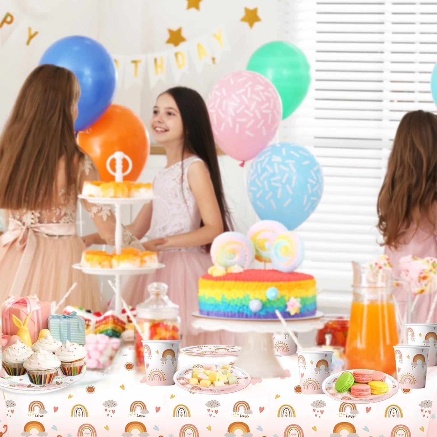Drei Kinder stehen an einem farbenfrohen Geburtstagstisch mit Luftballons, Kuchen und Süßigkeiten und feiern mit einem festlichen Banner im Hintergrund.