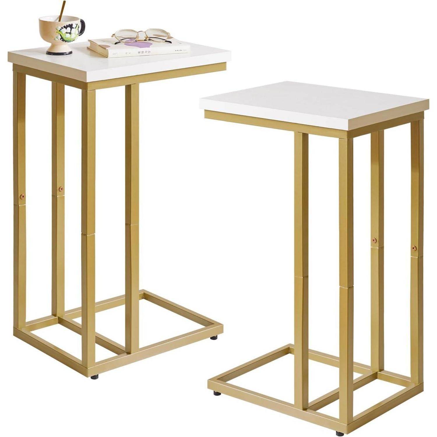 Zwei passende quadratische Beistelltische mit goldenen Metallrahmen und weißen Tischplatten; einer hält ein Buch und eine Tasse mit einem Löffel.