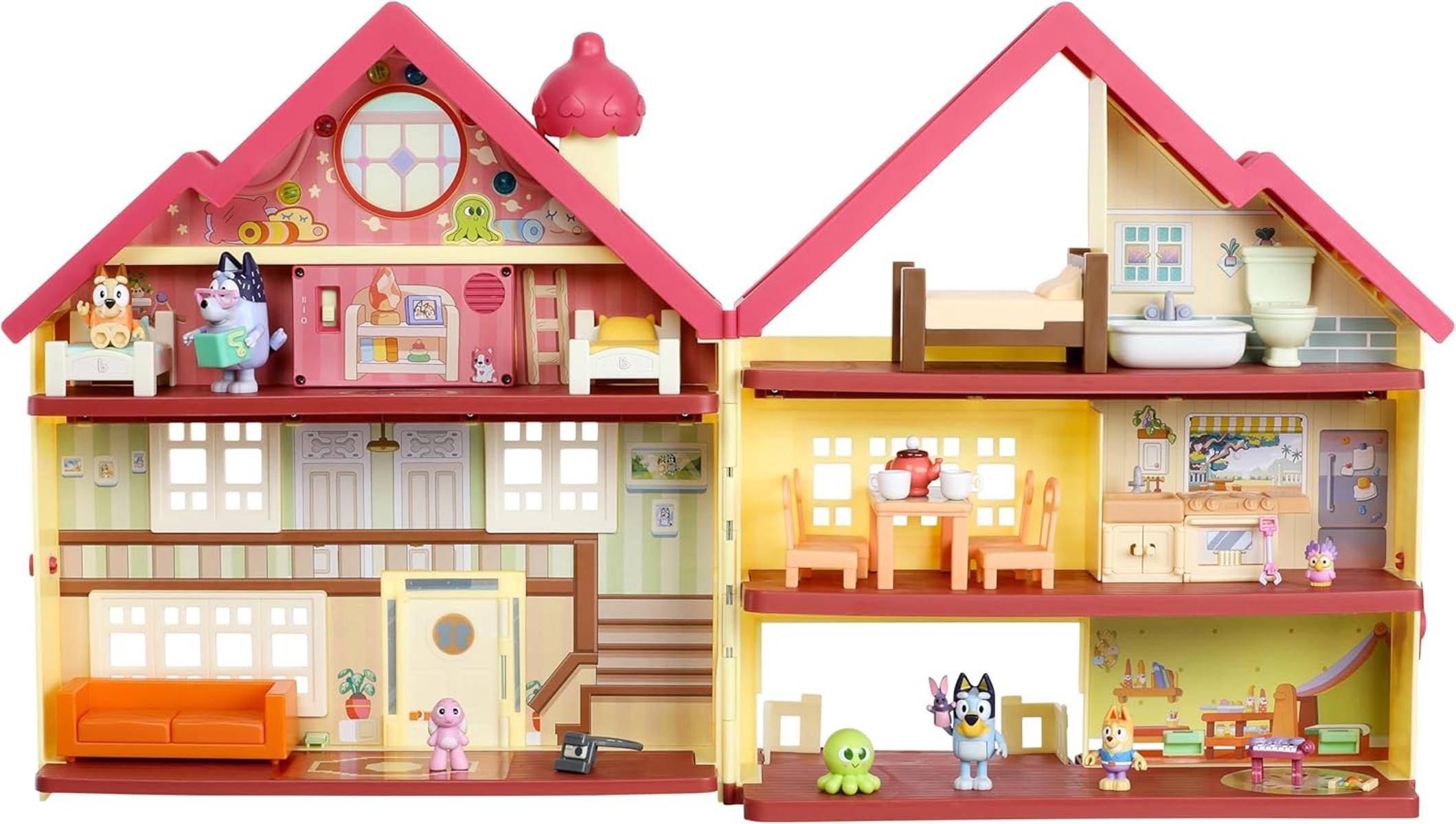 Ein farbenfrohes Puppenhaus mit rosa Dach, das möblierte Zimmer mit einem Schlafzimmer, Wohnzimmer und Küche aufweist und von Spielzeugfiguren bevölkert ist.