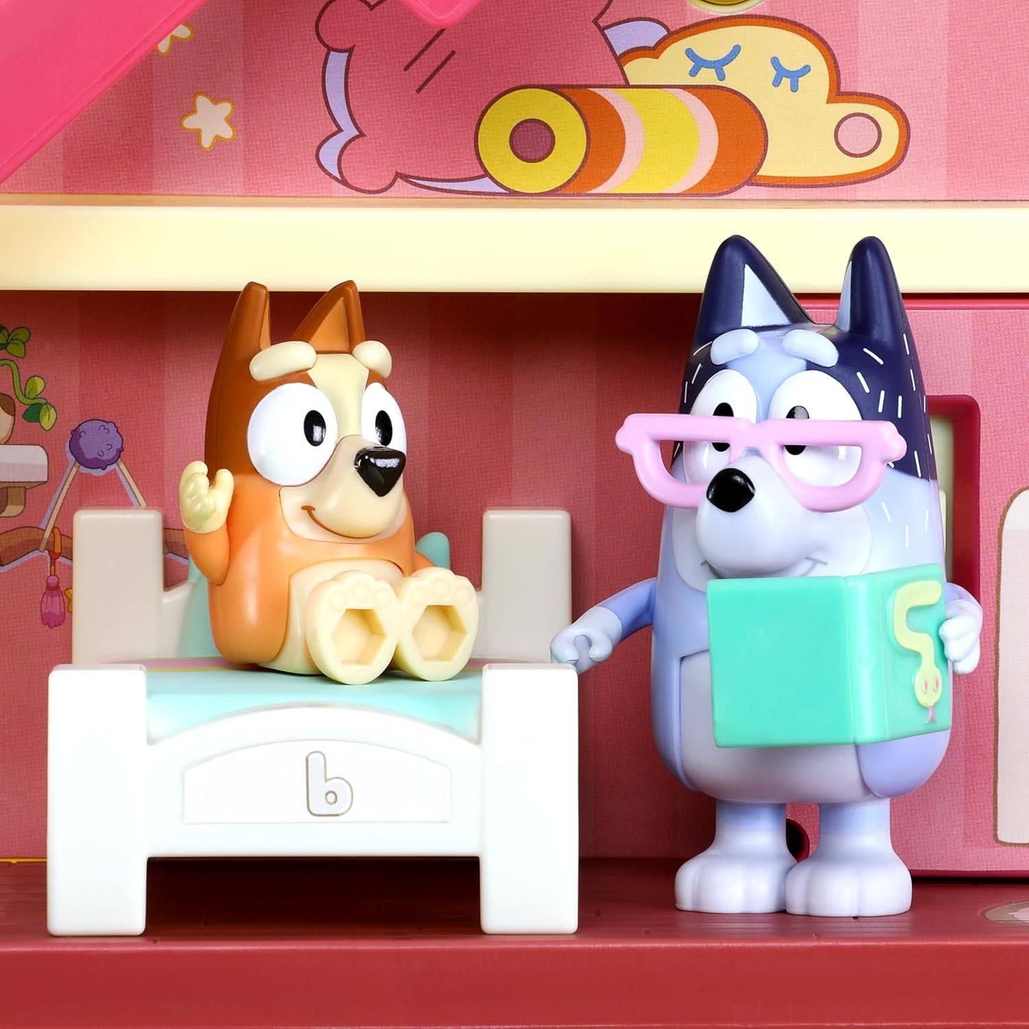 Zwei Spielzeugfiguren, die Hunden ähneln, in einem bunten Spielzimmer; eine hält ein Buch, und die andere sitzt auf einem Stuhl.