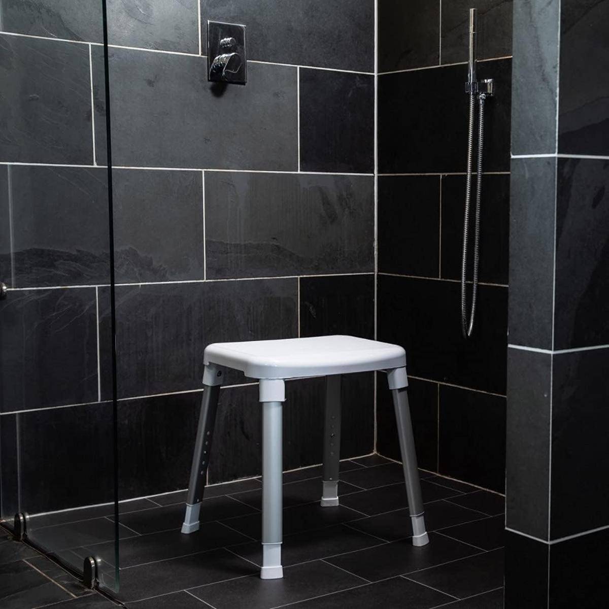 Ein gefliester Duschbereich mit einem weißen, verstellbaren Duschstuhl und einem an der Wand angebrachten Handbrausekopf.