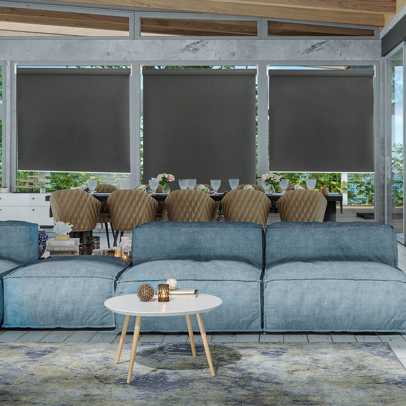 Ein modernes Wohnzimmer mit blauen Sofas, einem runden Couchtisch, dekorativen Kerzen und großen Fenstern mit geschlossenen Jalousien, die nur wenig Sonnenlicht hereinlassen.