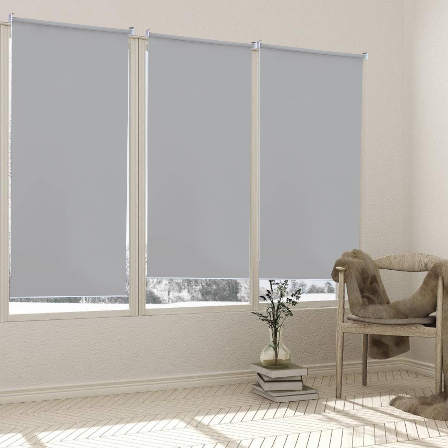 Drei hellgraue Rollos bedecken große Fenster in einem hellen Raum mit hellgestrichenen Wänden und Holzboden, mit einer kleinen Pflanze und einem gemütlichen Stuhl.