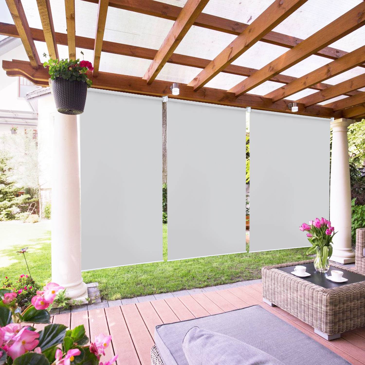 Eine Terrasse mit einer Pergola, Rattanmöbeln und hängenden Pflanzen. Weiße Sonnenschutzvorrichtungen spenden Schatten. Garten mit Grünflächen im Hintergrund.