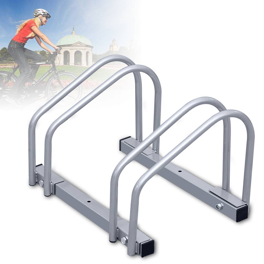 Ein Fahrradständer mit drei gewölbten Metallschleifen steht im Vordergrund. Im Hintergrund fährt eine Radfahrerin an einem historischen Gebäude vorbei.