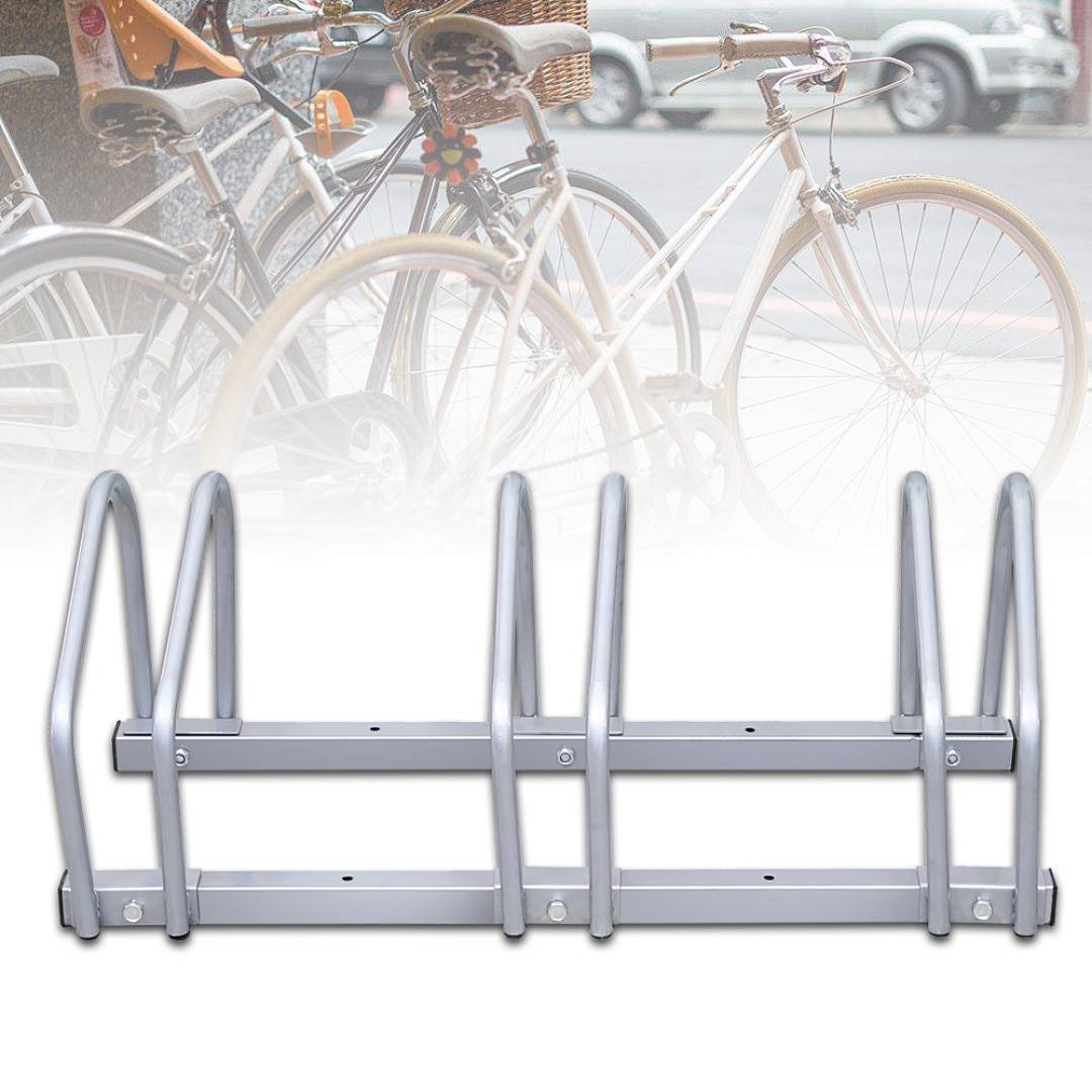Eine Reihe leerer silberner Fahrradständer im Vordergrund mit mehreren geparkten Fahrrädern auf der anderen Straßenseite im Hintergrund.
