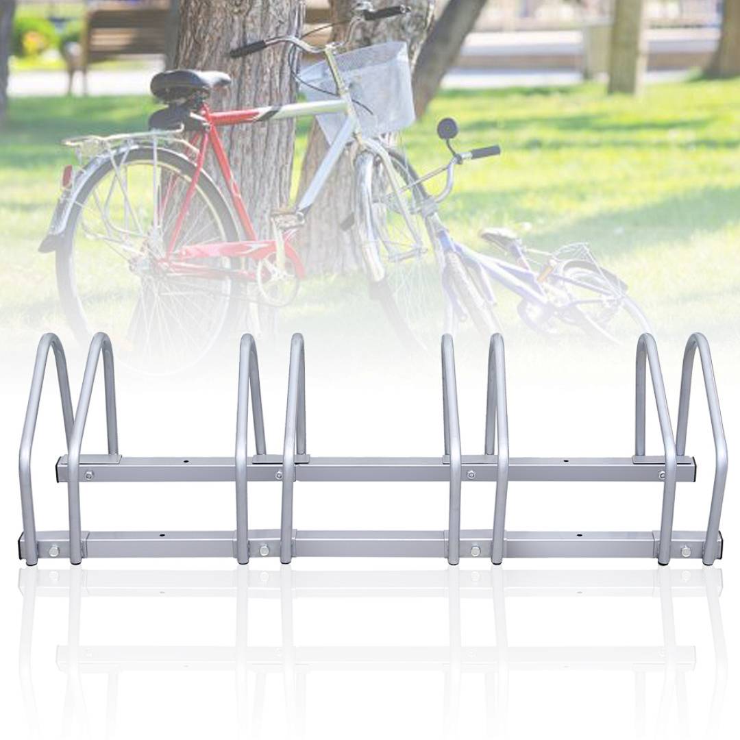 Ein silberner Fahrradständer mit Plätzen zum Abstellen von Fahrrädern, gezeigt vor einer unscharfen Parkszene mit Bäumen und Gras.