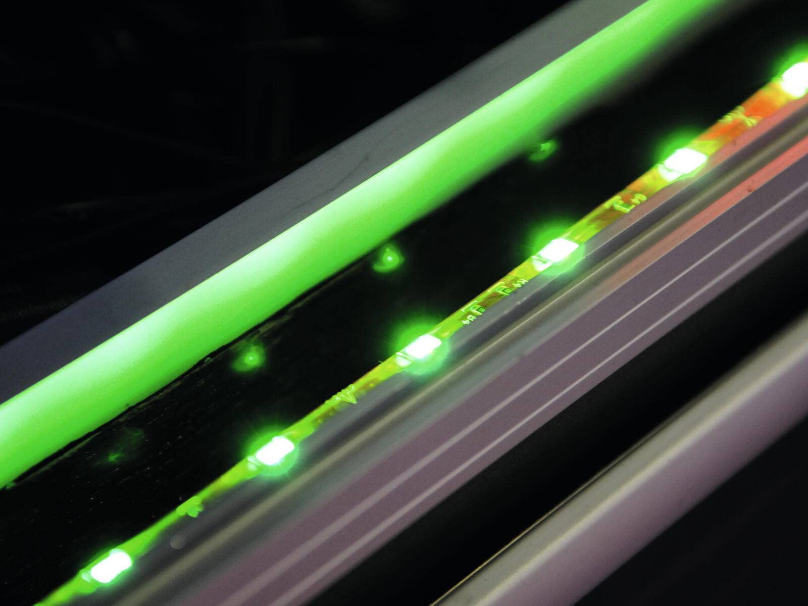 Nahaufnahme eines leuchtenden grünen LED-Streifenlichts vor dunklem Hintergrund, das moderne Beleuchtungstechnologie zeigt.