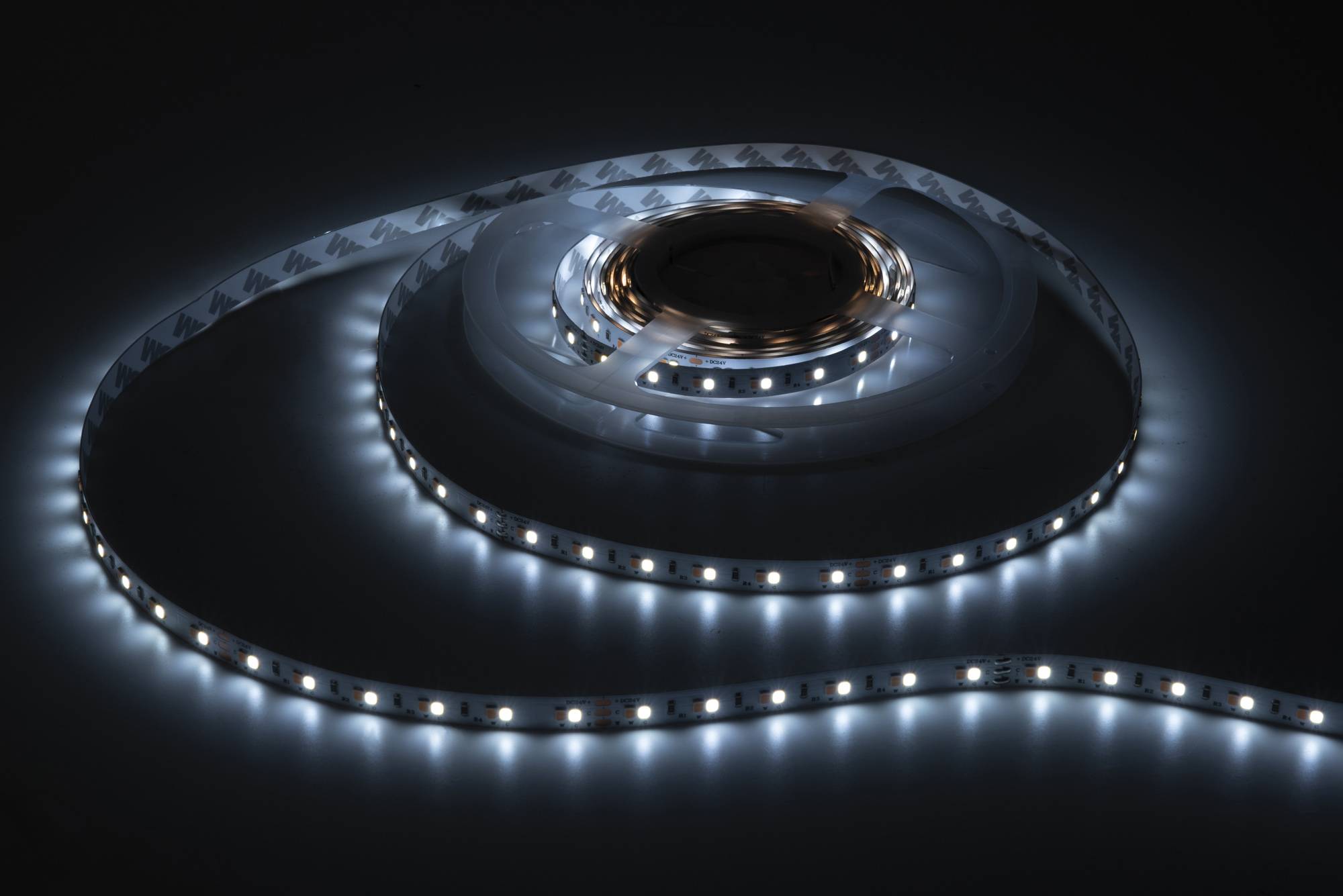 Ein aufgerolltes LED-Band gibt in einer gedimmten Umgebung ein kühles weißes Licht ab und zeigt seine Flexibilität und Helligkeit.