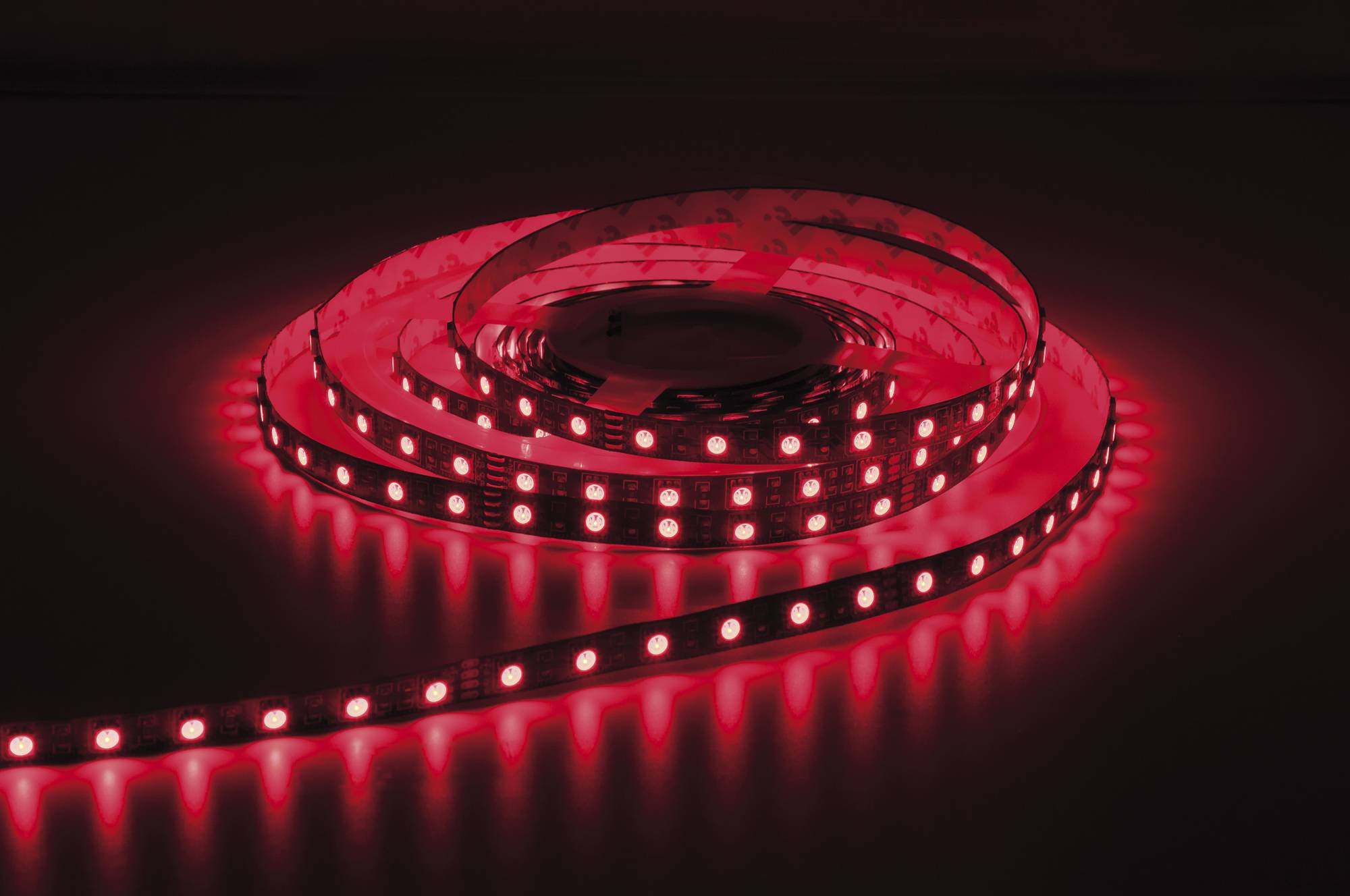 Ein leuchtender roter LED-Streifenlichter ist auf einer dunklen Oberfläche aufgewickelt und erleuchtet den Bereich mit warmem rotem Licht.