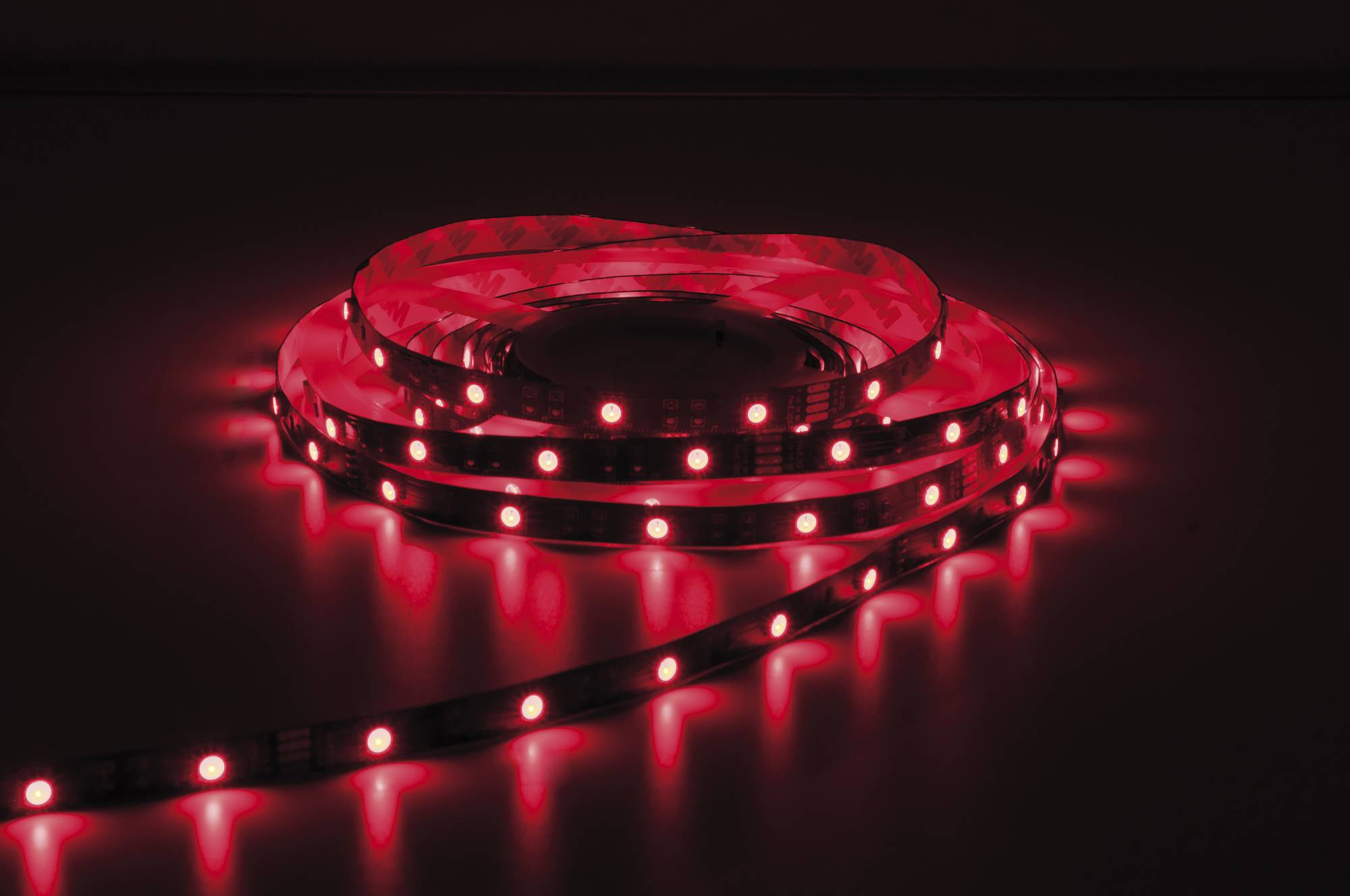 Ein aufgerollter Streifen roter LED-Leuchten leuchtet in einer dunklen Umgebung hell auf und beleuchtet die Umgebung mit leuchtendem rotem Licht.