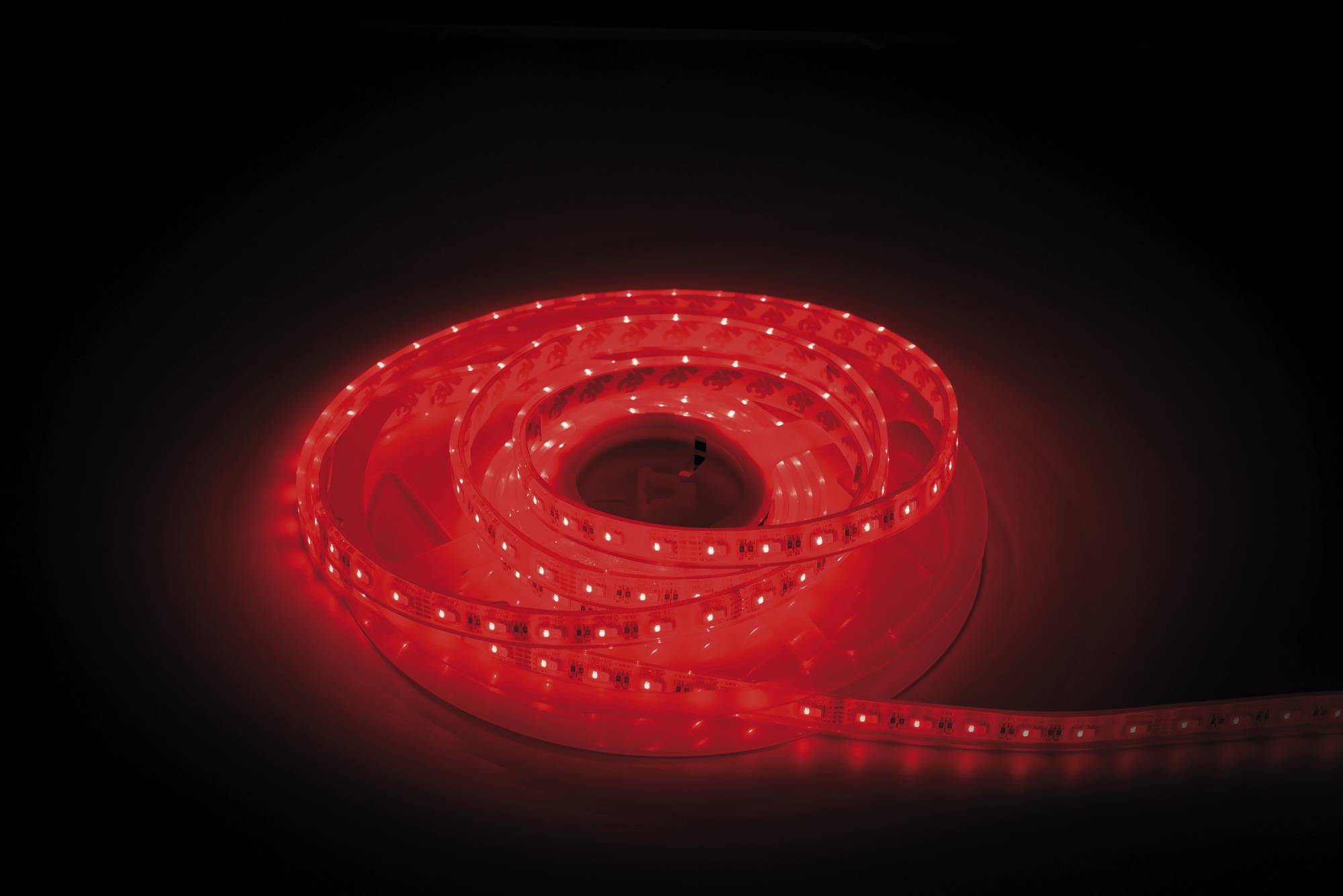 Aufgerollte rote LED-Streifenlichter, die vor dunklem Hintergrund leuchten und mehrere kleine helle LEDs entlang der Länge des Streifens zeigen.