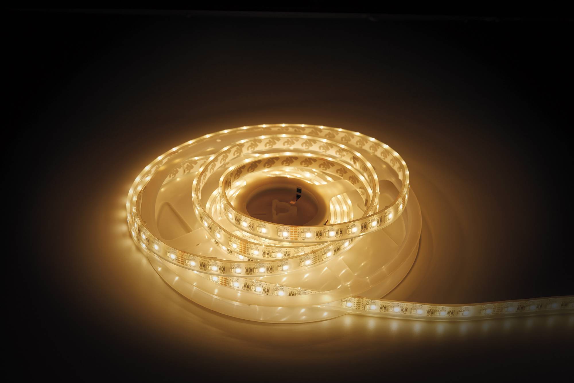 Ein aufgerollter Streifen aus warmweißen LED-Lichtern strahlt ein sanftes Glühen aus und ist auf einer dunklen Oberfläche platziert, wobei sein flexibles, beleuchtetes Design hervorgehoben wird.