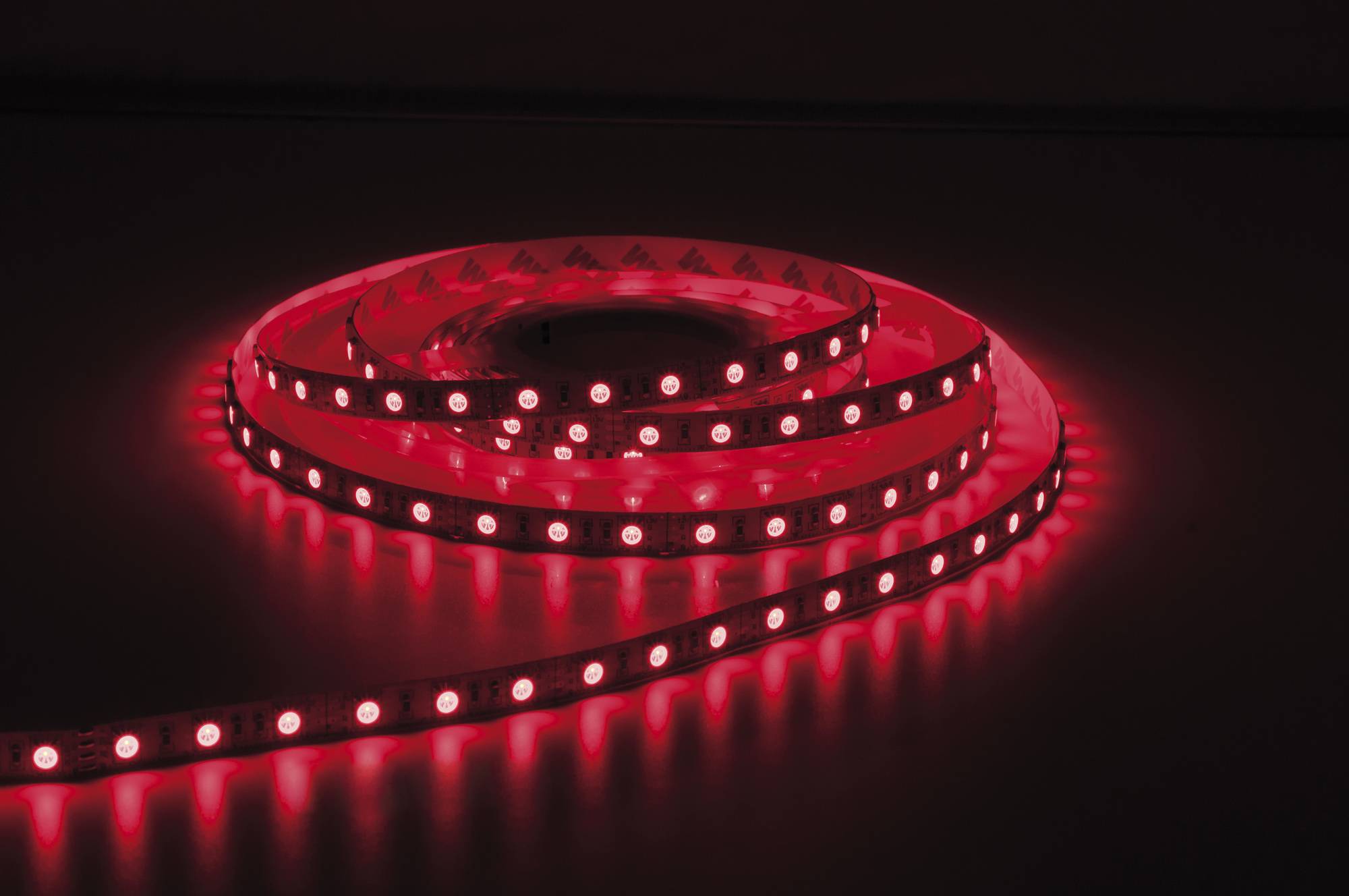 Ein aufgerolltes rotes LED-Streifenlicht, das im Dunkeln leuchtet und seine Umgebung mit einem sanften roten Farbton beleuchtet.